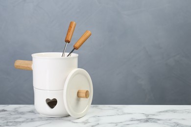 Fondue set on white marble table against light grey background, space for text