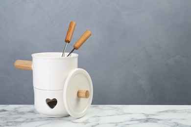 Photo of Fondue set on white marble table against light grey background, space for text