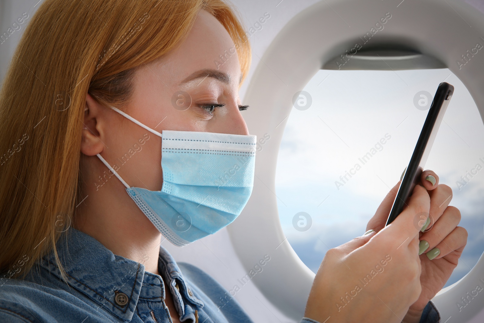 Image of Traveling by airplane during coronavirus pandemic. Woman with face mask and phone near porthole