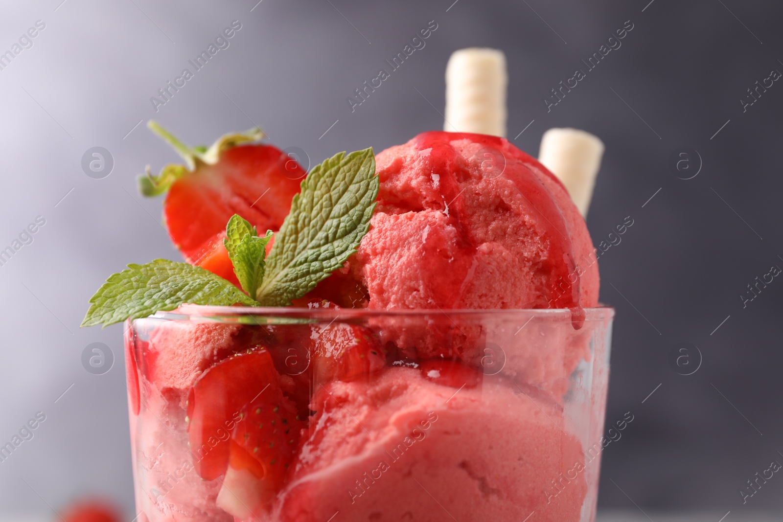 Photo of Tasty strawberry ice cream with fresh berries and wafer rolls in glass dessert bowl against grey background, closeup