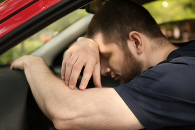 Tired man sleeping on steering wheel in his car