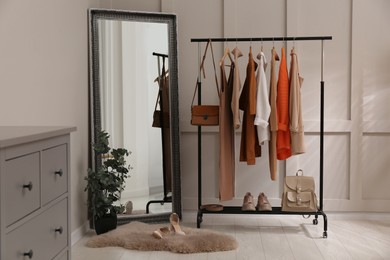 Photo of Rack with stylish women's clothes and mirror in dressing room