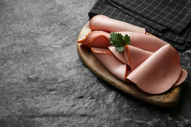 Photo of Board with slices of tasty boiled sausage and parsley on dark textured table. Space for text