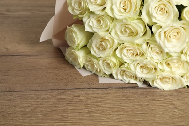 Photo of Luxury bouquet of fresh roses on wooden table, space for text