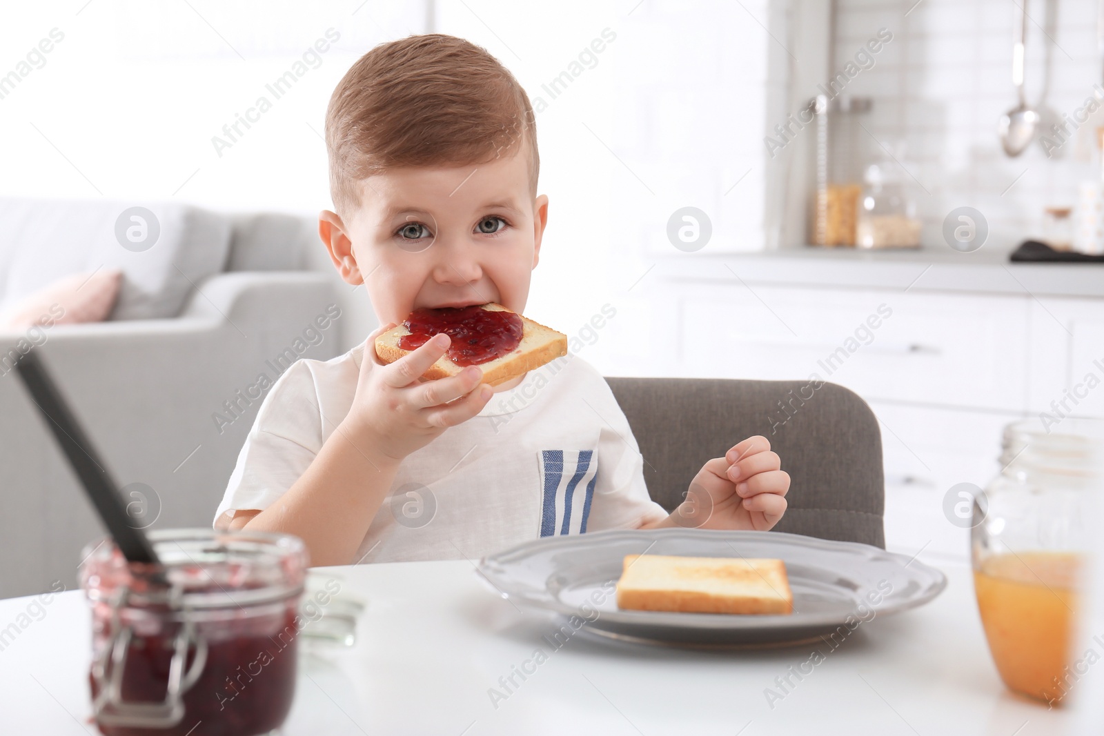 Photo of Cute little boy eating toast with sweet jam at table