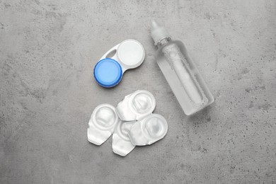 Packages with contact lenses, case and drops on grey table, flat lay