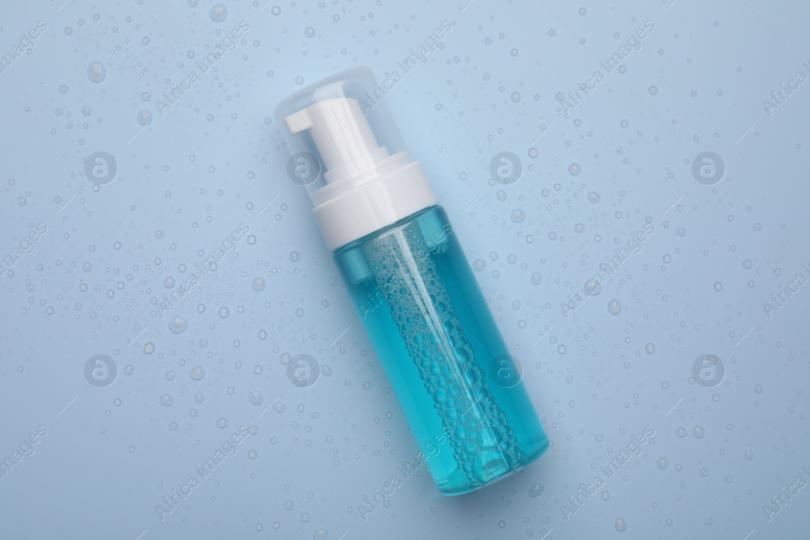 Photo of Wet bottle of face cleansing product on light blue background, top view