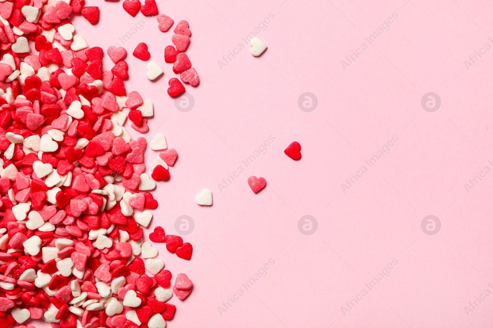 Photo of Heart shaped sprinkles on pink background, flat lay. Space for text