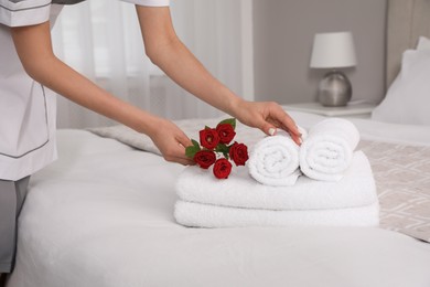 Photo of Chambermaid putting flowers with fresh towels in hotel room, closeup