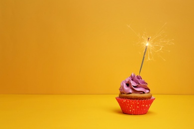 Photo of Birthday cupcake with sparkler on color background