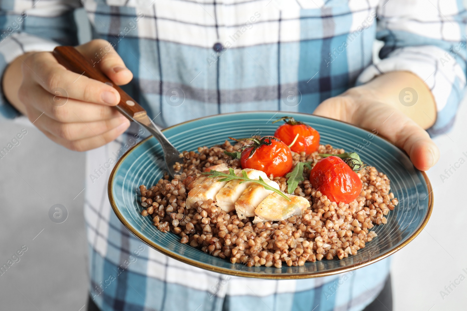 Photo of Woman holding plate of buckwheat porridge with meat and tomatoes, closeup