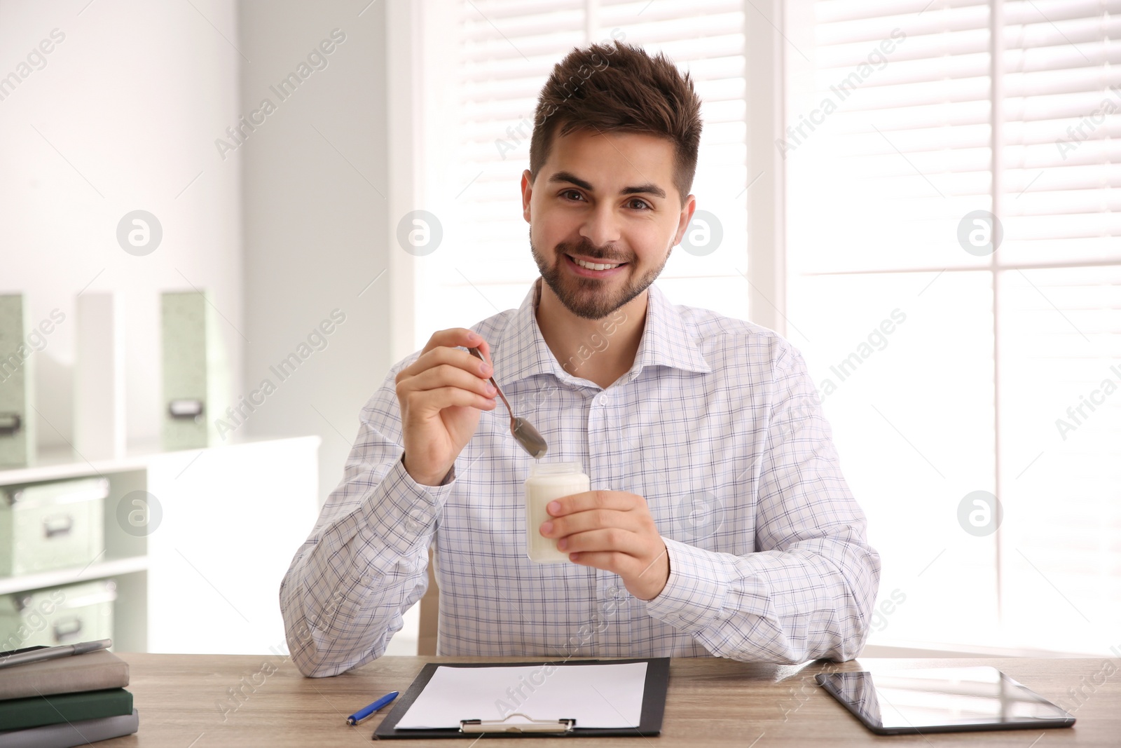 Photo of Happy young man with tasty yogurt in office