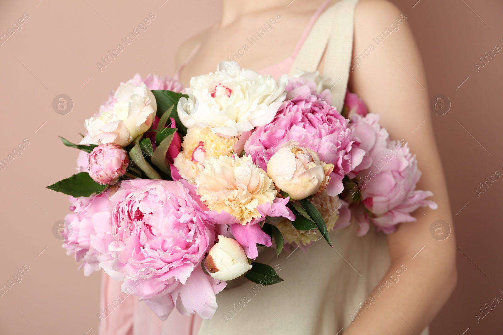 Photo of Woman with bouquet of beautiful peonies in bag on beige background, closeup