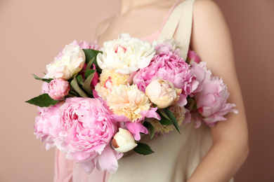 Woman with bouquet of beautiful peonies in bag on beige background, closeup