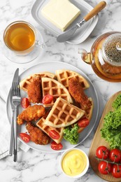 Photo of Tasty Belgian waffles served with fried chicken, tomatoes, lettuce and tea on white marble table, flat lay