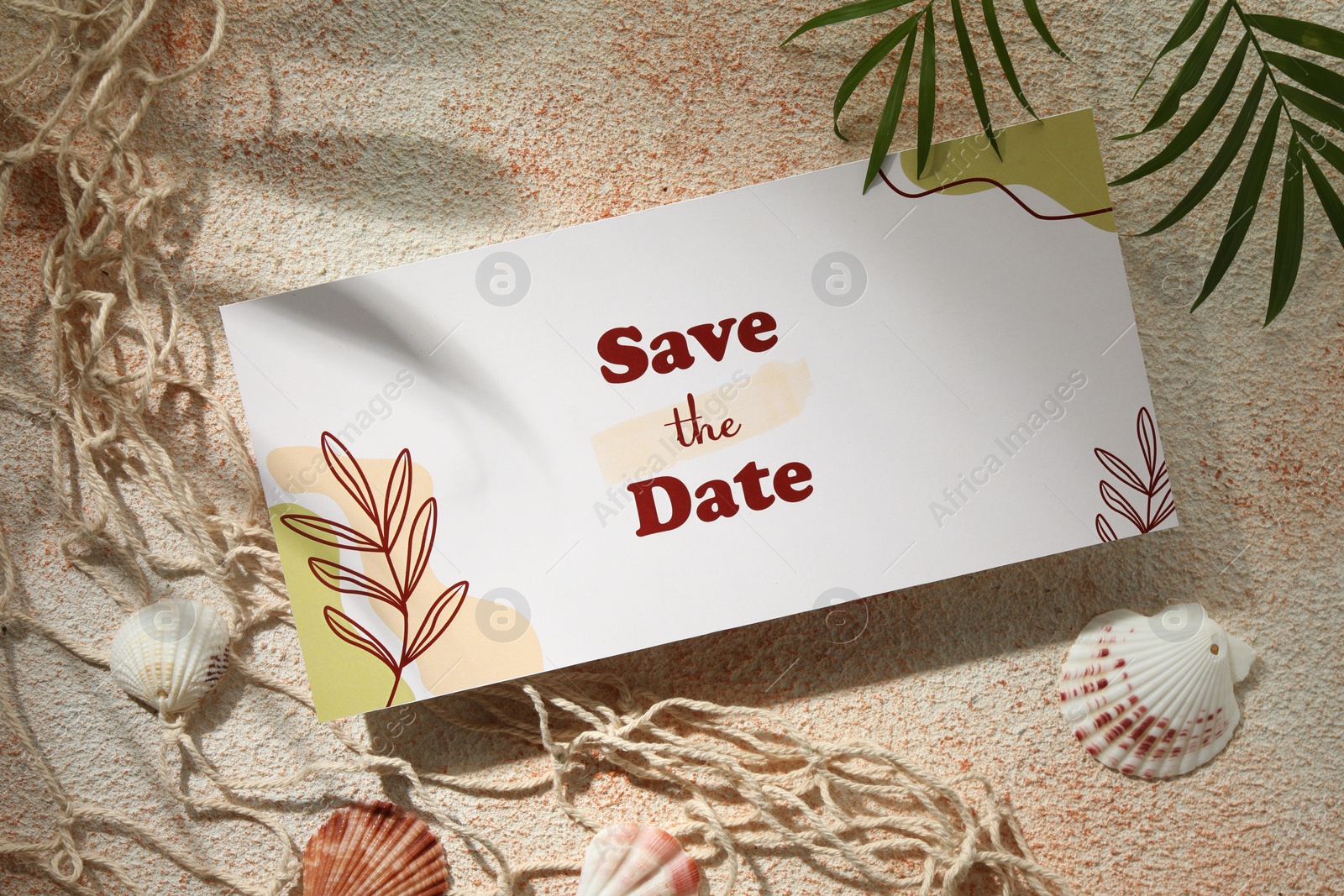 Photo of Beautiful wedding invitation card with Save the Date phrase, seashells, net and green leaves on textured beige background, flat lay