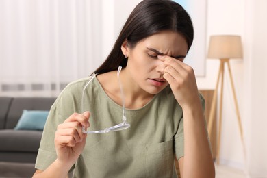 Photo of Sad woman with eyeglasses suffering from headache indoors