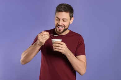 Photo of Handsome man with tasty yogurt on purple background