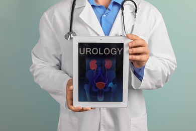 Male doctor holding tablet with urinary system on screen against color background