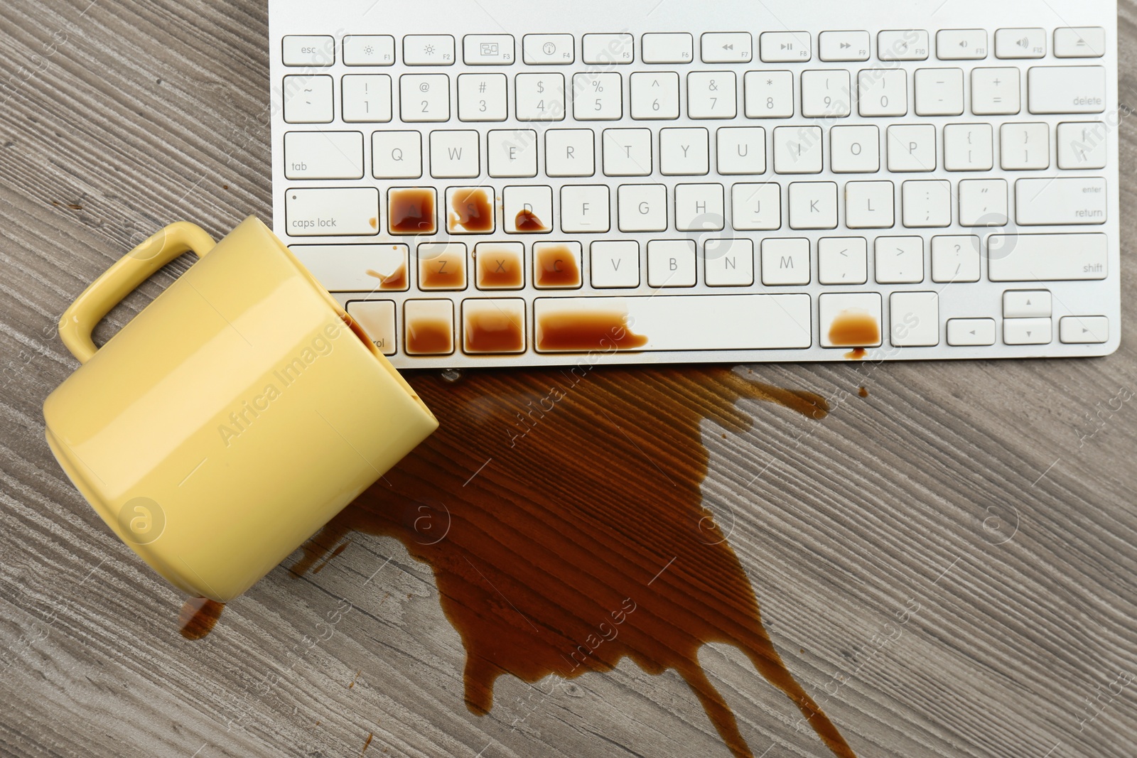 Photo of Cup of coffee spilled over computer keyboard on wooden table, flat lay