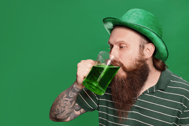 Photo of Bearded man drinking green beer on color background. St. Patrick's Day celebration