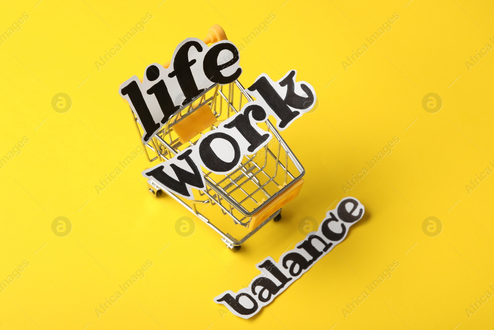 Photo of Toy shopping cart on yellow background, above view. Life work balance concept