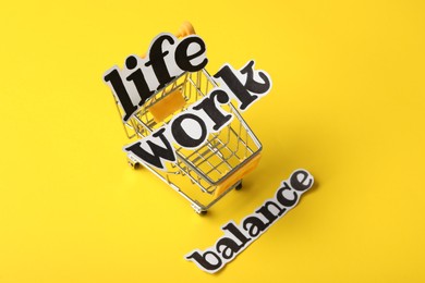 Photo of Toy shopping cart on yellow background, above view. Life work balance concept