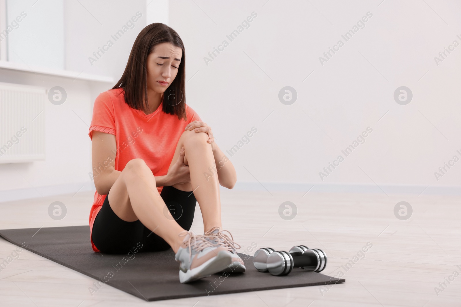 Photo of Young woman suffering from leg pain on exercise mat indoors, space for text