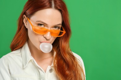 Photo of Beautiful woman in sunglasses blowing bubble gum on green background. Space for text