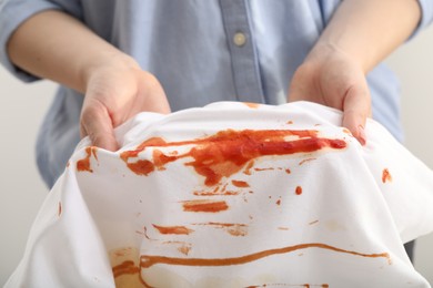 Photo of Woman showing stain from sauce on shirt against light grey background, closeup