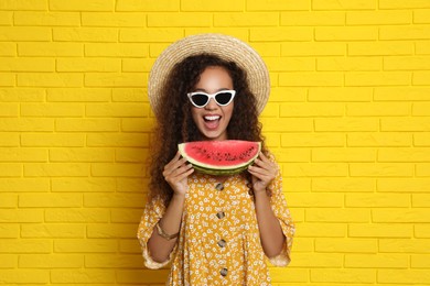 Photo of Beautiful young African-American woman with watermelon near yellow brick wall