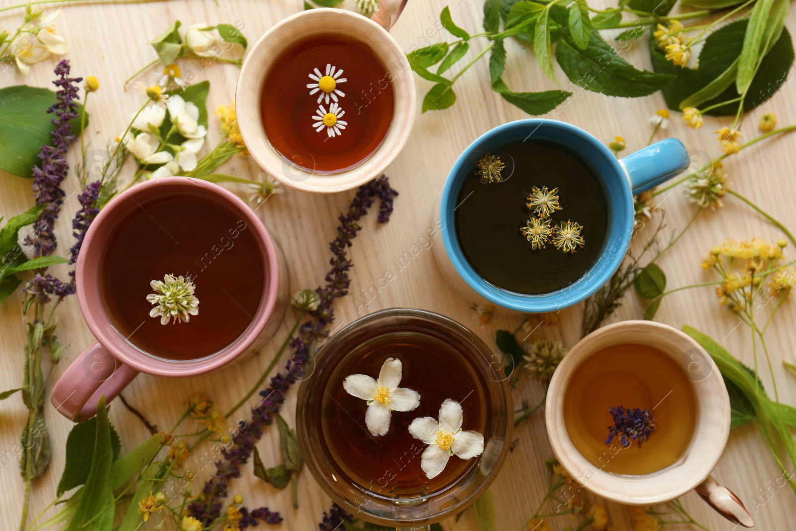 Photo of Different cups of hot aromatic tea and fresh herbs on white wooden table, flat lay