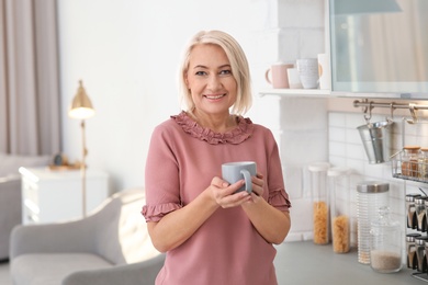 Portrait of beautiful mature woman with cup in kitchen