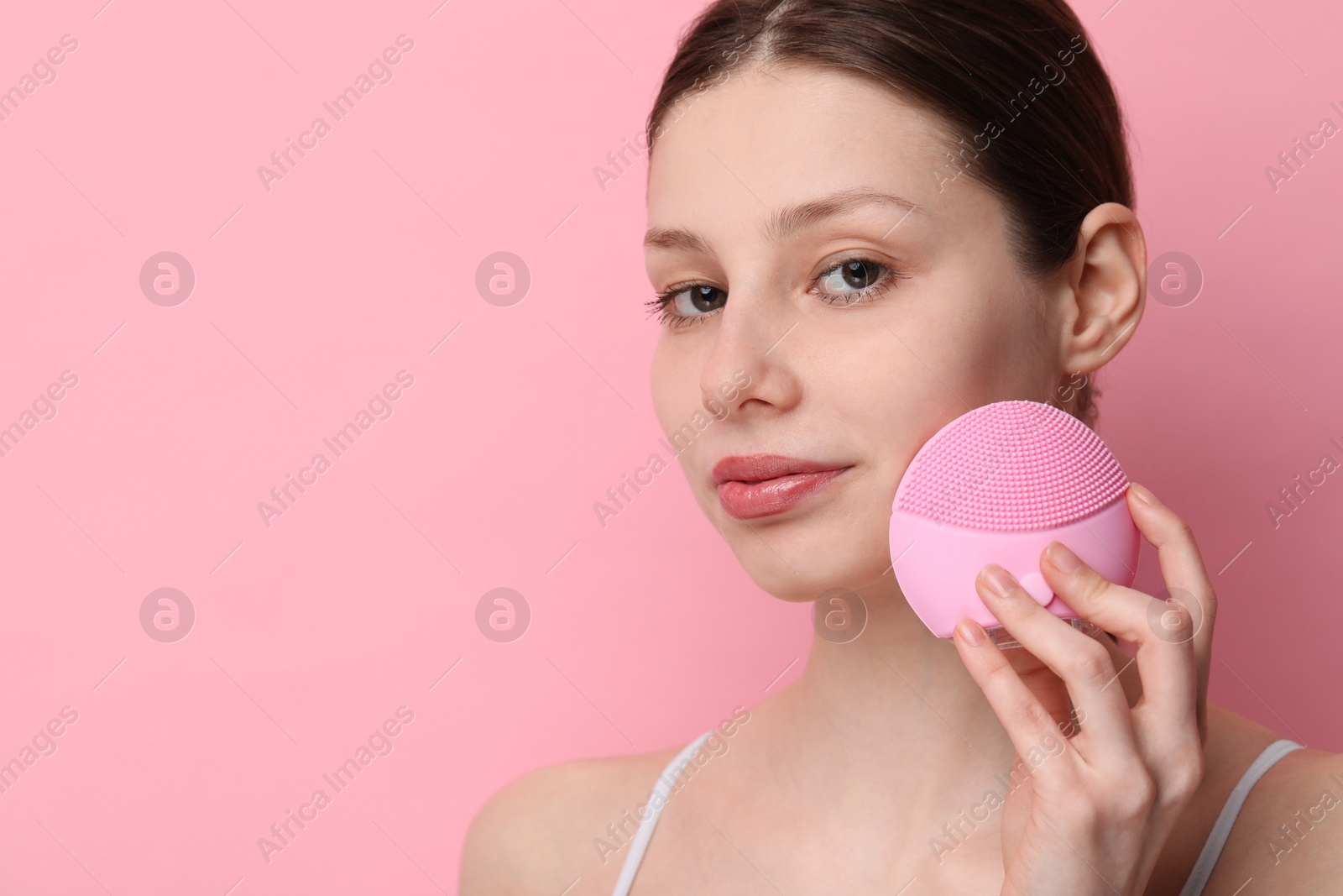 Photo of Washing face. Young woman with cleansing brush on pink background, space for text