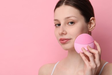 Washing face. Young woman with cleansing brush on pink background, space for text