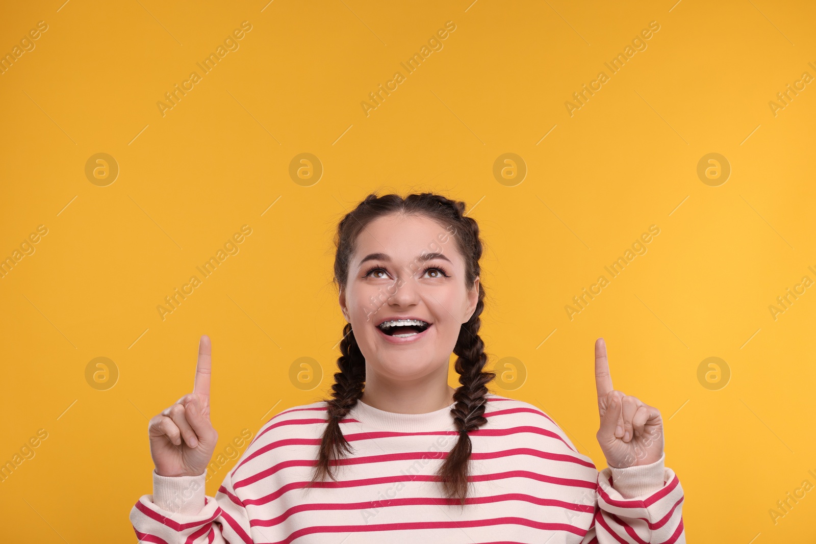 Photo of Happy woman with braces pointing at something on orange background. Space for text
