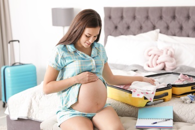 Photo of Pregnant woman packing suitcase for maternity hospital at home