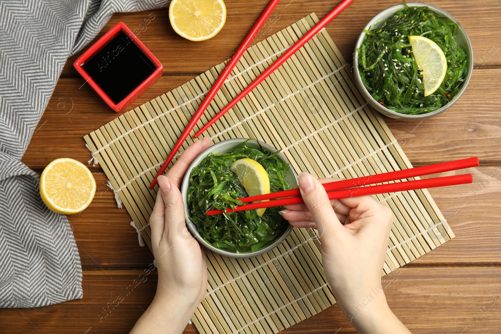 Photo of Woman eating Japanese seaweed salad at wooden table, top view