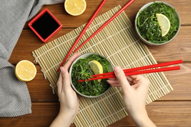 Photo of Woman eating Japanese seaweed salad at wooden table, top view