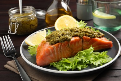 Photo of Delicious cooked salmon with pesto sauce, lettuce and lemon on wooden table, closeup