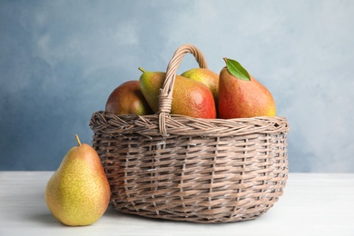 Photo of Ripe juicy pears in wicker basket on white wooden table against blue background