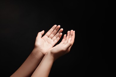 Photo of Woman stretching hands towards light in darkness, closeup
