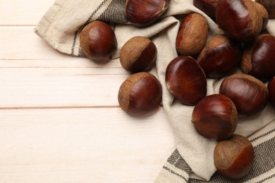 Photo of Sweet fresh edible chestnuts on light wooden table, top view. Space for text