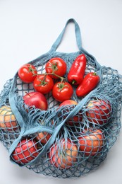 Photo of String bag with vegetables and apples on light grey background, top view