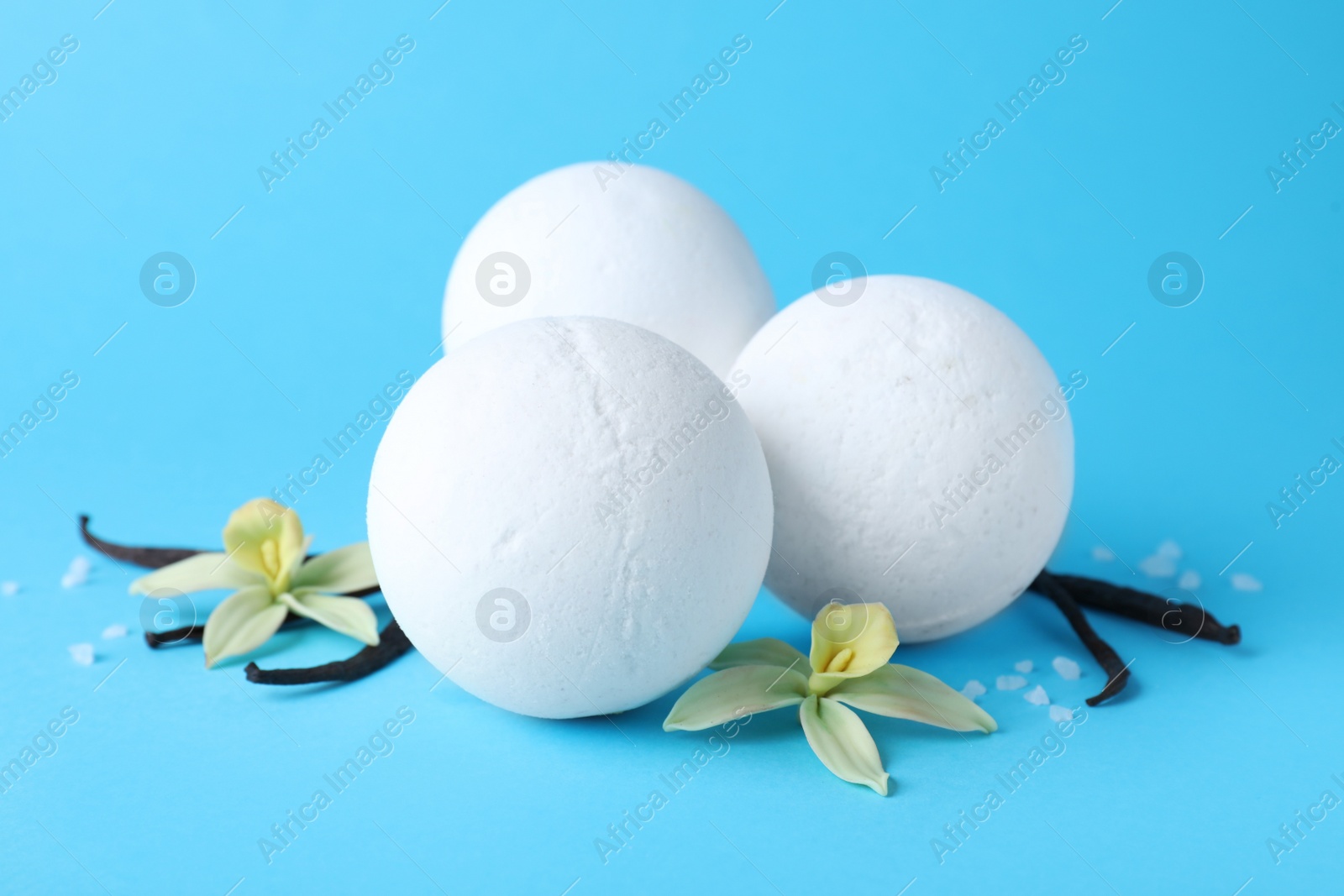 Photo of White bath bombs, vanilla sticks and flowers on light blue background