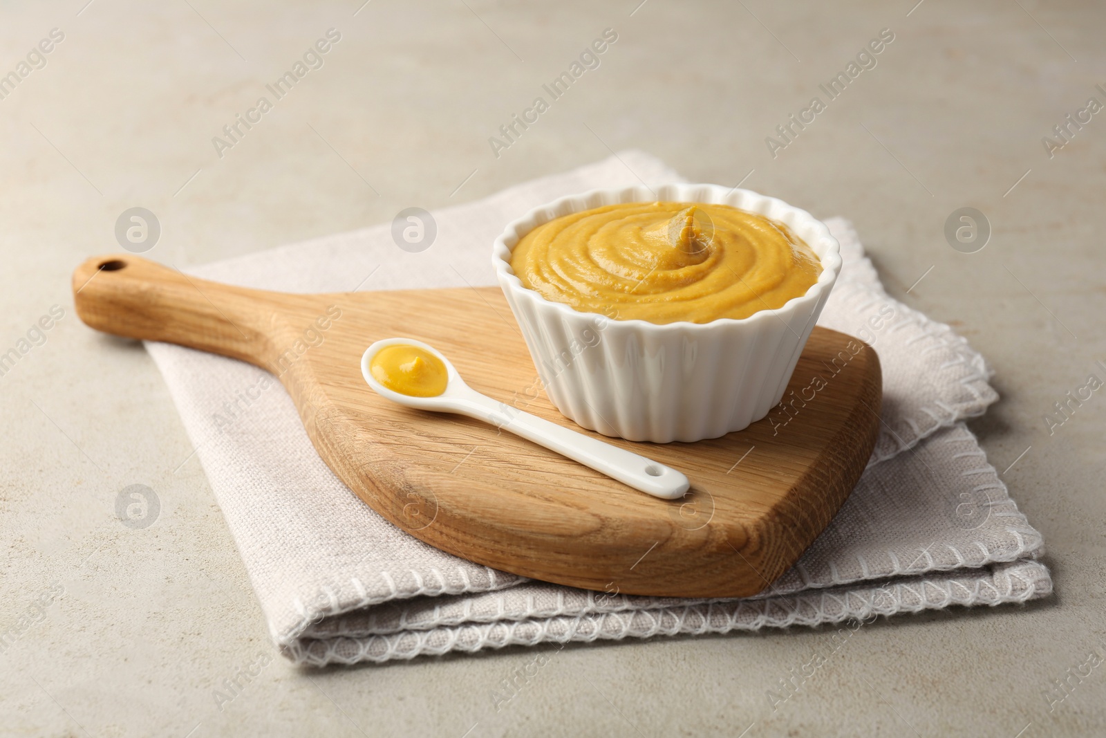 Photo of Bowl and spoon with tasty mustard sauce on light textured table