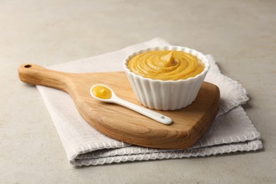 Bowl and spoon with tasty mustard sauce on light textured table