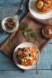 Tasty pancakes with berries, nuts and syrup on table, top view