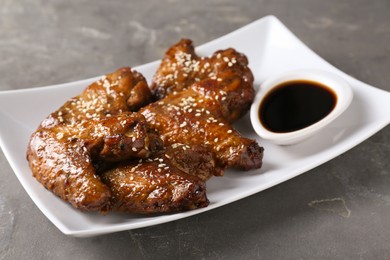 Photo of Glazed chicken wings and soy sauce on grey table, closeup