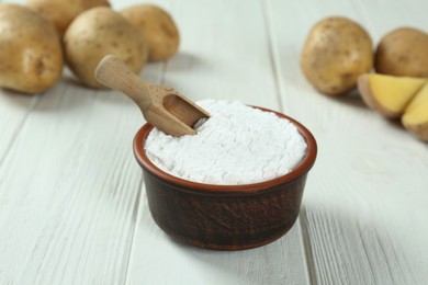 Photo of Bowl with starch, scoop and fresh potatoes on wooden table